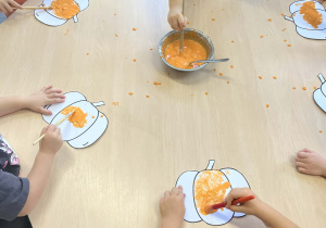 Dzieci przy stoliku malujący wzór dyni pomarańczową magiczną farbą