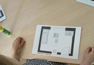 Dziewczynka projektuje na kartonie ustawienie mebli w pokoju dziecięcym