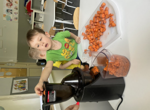 chłopiec wrzuca pokrojoną marchewkę do wyciskarki