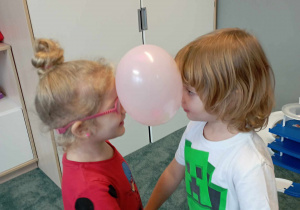 Chłopiec i dziewczynka tańczą z balonem między głowami