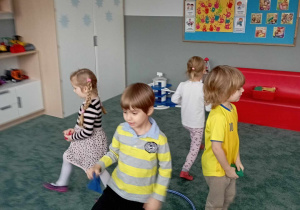 Dzieci podczas zabawy "Kto szybszy?" oddalają się od koła hula hop, by za chwilę odwrócić się i wrzucić woreczek do koła