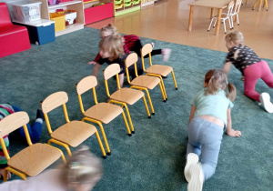 Dzieci poruszają się na czworakach wokół ustawionych na dywanie krzeseł