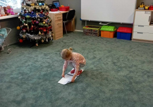 Dziewczynka kładzie przed sobą na dywanie kartkę A4, by móc kontynuować spacer po kartkach
