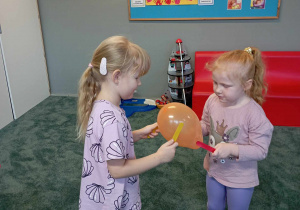 Dziewczynki łapią balon za pomocą drewnianych patyczków