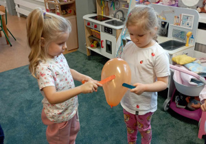 Dziewczynki podają sobie balonik za pomocą drewnianych patyczków