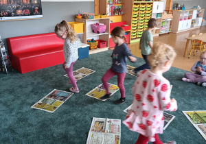 Dzieci chodzą między gazetami rozłożonymi na dywanie
