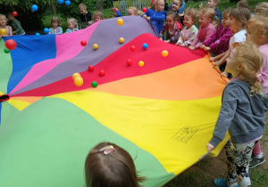 Dzieci podczas zabawy chustą animacyjną i kolorowymi piłeczkami