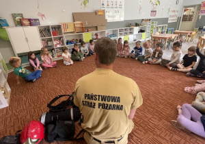 Dzieci na dywanie słuchają Taty Jagody który, opowiada o pracy strażaka