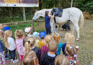 dzieci przyglądają się jak strażniczka zakłada koniowi siodło