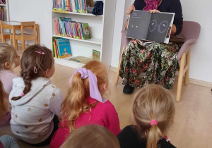 Dzieci oglądają ilustrację w książce "10 kotów" trzymanej przez jej autorkę