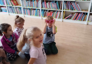 Chłopiec przymierza różowe okulary. Obok niego siedzą dziewczynki czekające na swoją kolej