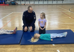 Dziewczynka wraz z policjantem układają dziewczynkę w pozycji bocznej bezpiecznej