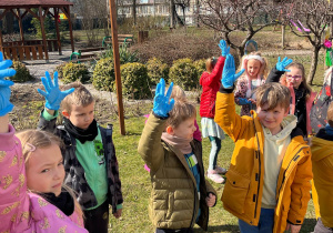 Dzieci w ogrodzie przedszkolnym w rękawiczkach jednorazowych przygotowujące się do sprzątania świata