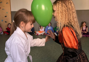 Dziewczynki w strojach karnawałowych podczas zabawy na sali gimnastycznej, tańczącej z balonem pomiędzy głowami