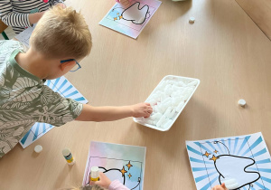Dzieci przy stoliku wykonują pracę plastyczną