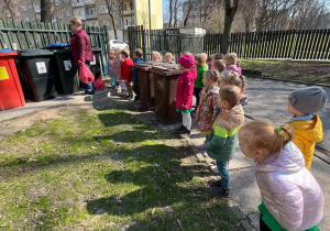 Dzieci przyglądają się nauczycielce, która wrzuca worek ze śmieciami do kosza