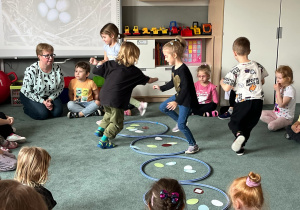 Dzieci podczas zabawy ruchowej w podrzucanie jaj do gniazd (kół hula hop)