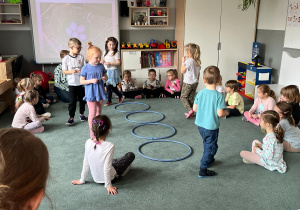 Dzieci podczas zabawy ruchowej w podrzucanie jaj do gniazd (kół hula hop)