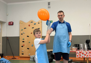 Chłopiec z panem trzymają butelkę z suchym lodem, dzięki któremu napompowuje się umieszczony na butelce balon