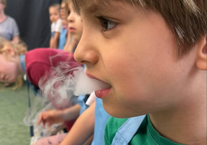 Chłopiec z unoszącym się z ust dymem ze spożywanego dymiącego smoczego chrupka