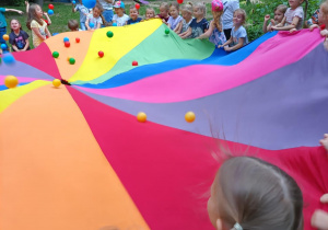 Dzieci podczas zabawy chustą animacyjną i kolorowymi piłeczkami