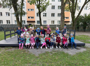dzieci w kurtkach siedzące na scenie w ogrodzie