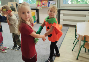 Dziewczynki tańczące ze sobą za ręce na dywanie w strojach jesiennych