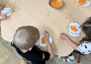 Dzieci przy stoliku malują magiczną farbą kolorowanki ze wzorem dyni