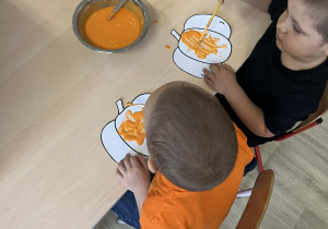 Chłopcy przy stoliku malują farbą kolorowanki ze wzorem dyni