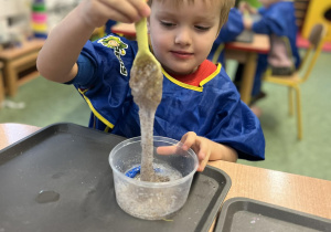 Chłopiec mieszający masę na slime w plastikowym pudełku