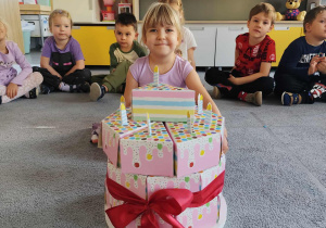 Dziewczynka z prezentami w kształcie tortu siedząca na dywanie