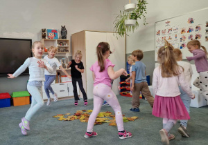 Dzieci tańczą dookoła rozrzuconych na dywanie jesiennych liści