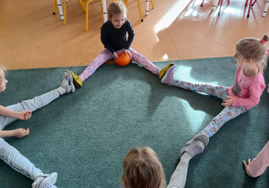 Dziewczynki siedzą na dywanie i turlają do siebie dynię
