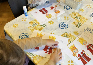 Dziewczynki przyklejają szaty królewskie na postaciach króla i królowej