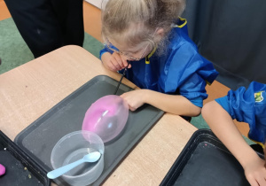 Dziewczynka nadmuchuje balon z własnoręcznie stworzonej masy sensorycznej