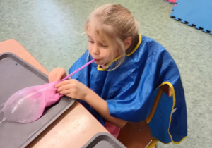 Dziewczynka nadmuchuje balon z własnoręcznie stworzonej masy sensorycznej