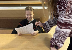 Pani Sędzia tłumaczy dziewczynce, wcielającej się w rolę prokuratora, jak odczytać akt oskarżenia