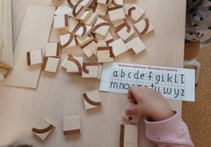 Dziewczynka podczas konstruowania z klocków małej litery pisanej i