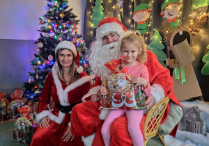 Zdjęcie dziewczynki pozowane z Mikołajem w świątecznej aranżacji