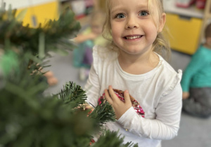 Dziewczynka ubierająca choinkę w sali uśmiechającą się do zdjęcia