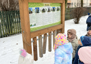 Dzieci grające na kawałkach drewna - tablica edukacyjna w ogrodzie przedszkolnym