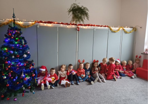 Dzieci siedzą na dywanie przy choince