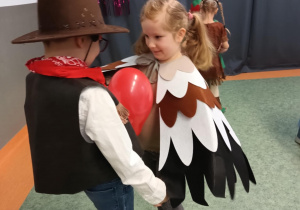 Dziewczynka i chłopiec tańczą z balonem trzymając go między brzuchami