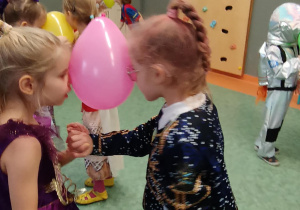 Dziewczynki tańczą z balonem trzymając go między głowami