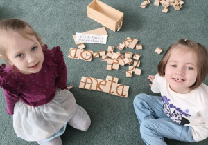 Dziewczynki pozują do zdjęcia z ułożonym z klocków wyrazem "meta"