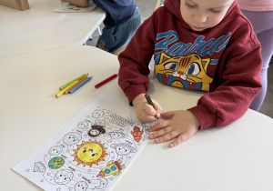 dzieci przy stołach wykonują karty pracy