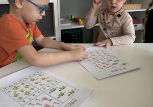 dzieci przy stołach wykonują karty pracy