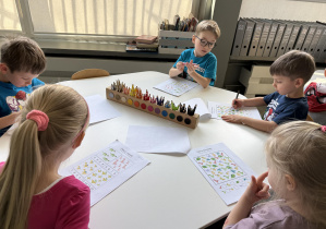 dzieci przy stołach wykonują karty pracy