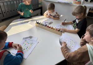 dzieci przy stołach wykonują karty pracy
