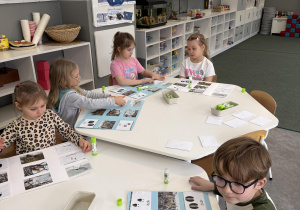 dzieci przy stołach wykonują karty pracy